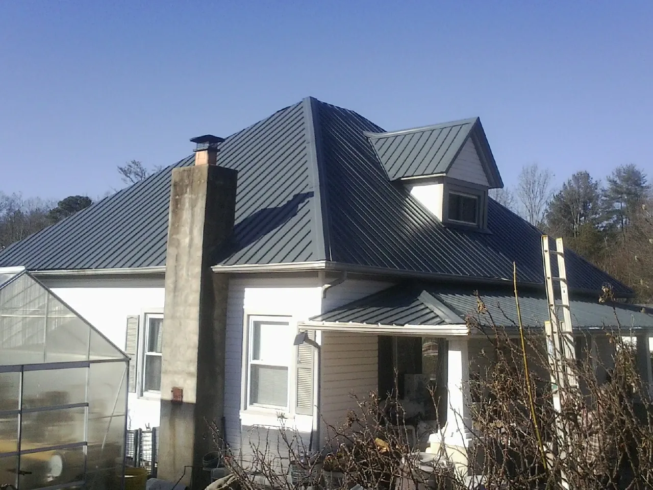 Dark blue standing seam metal roof on a white farmhouse with dormer — Slate & Tile Roof Repair by Roofing Brothers in East Pembroke