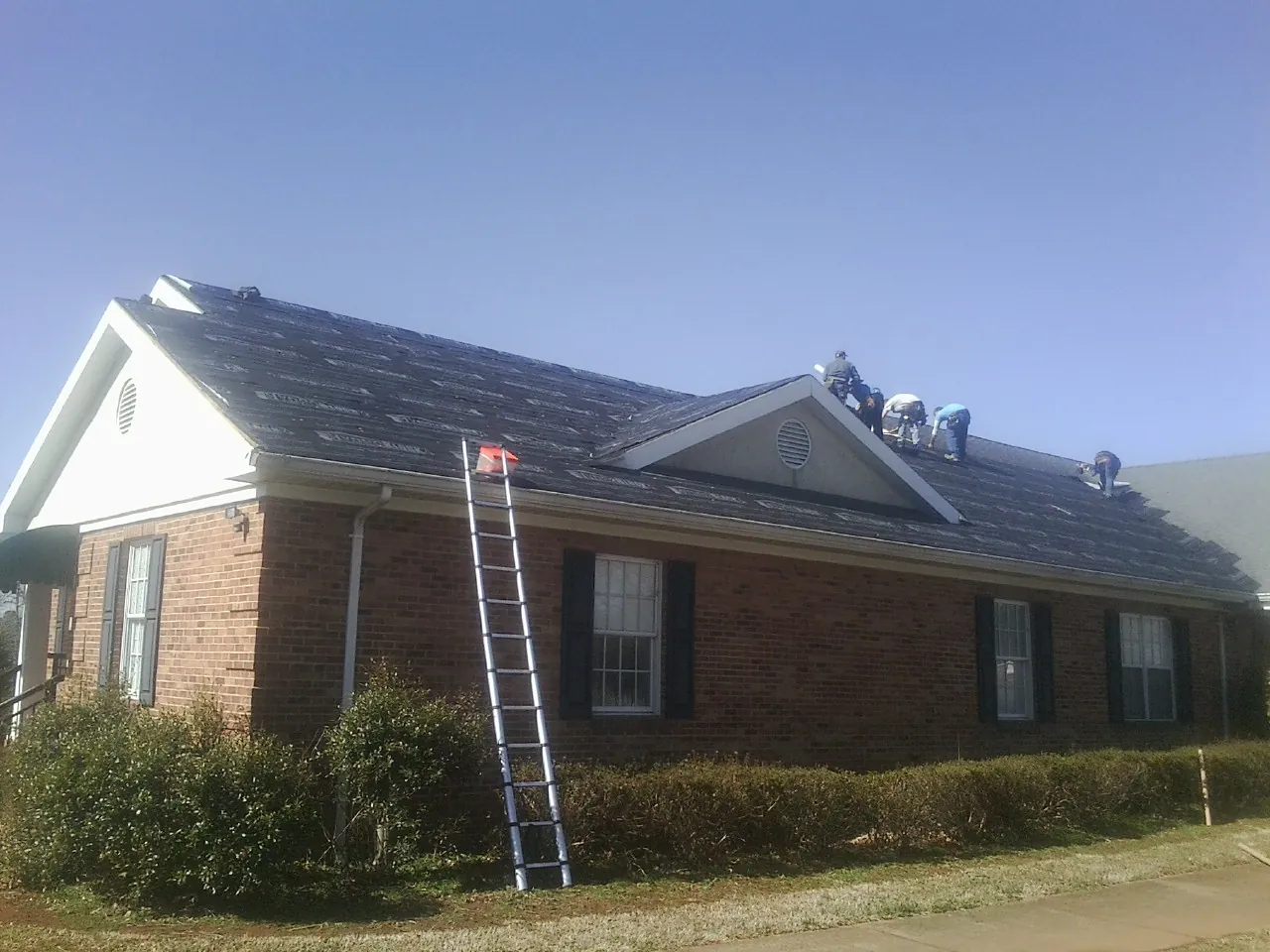 Crew tearing shingles off a brick ranch roof with a ladder set — Metal Roof Repair work by our crew in East Pembroke