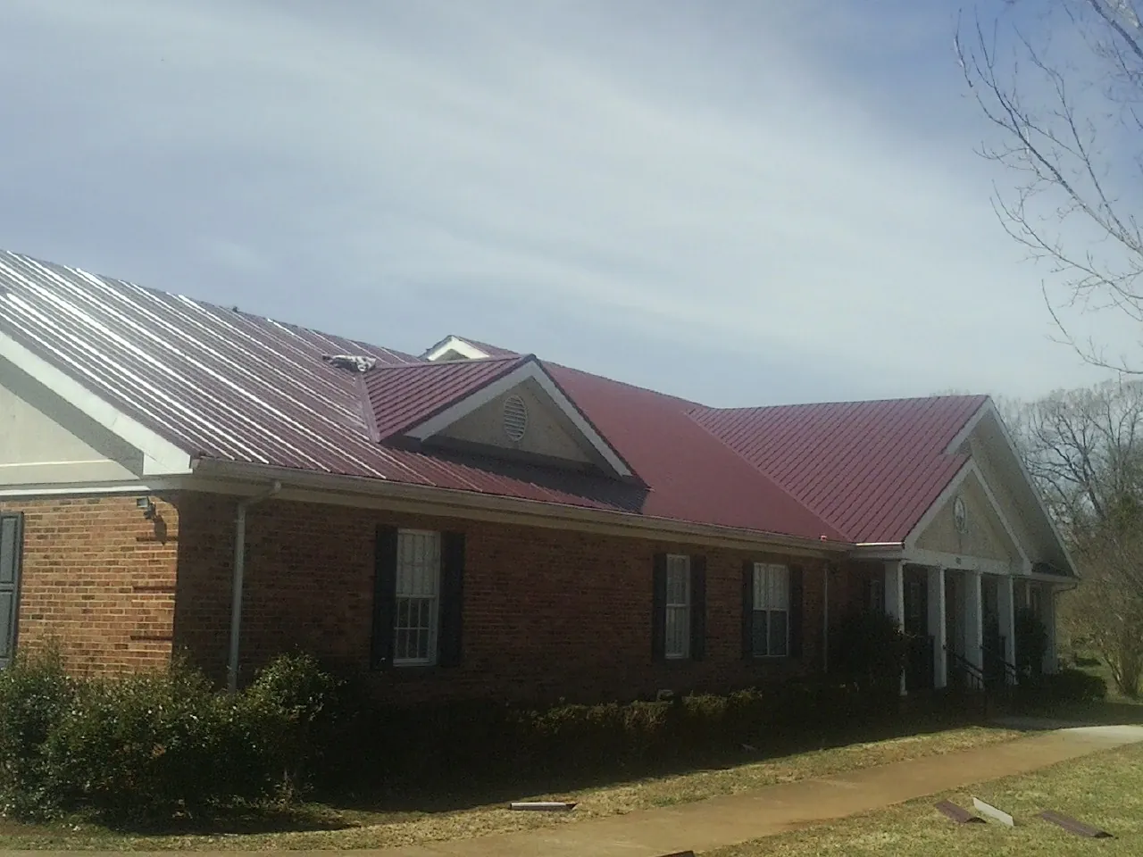 Red metal roof with gabled entries on a long brick building, from a Hail Damage Roof Repair job in East Pembroke