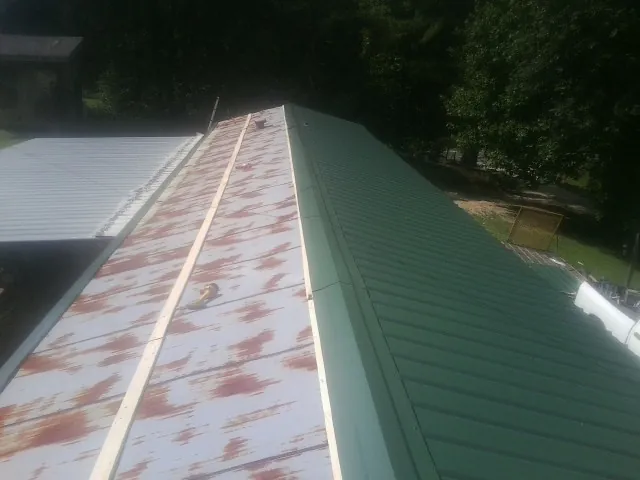 Old rusted panels beside newly installed green metal roofing — Wind Damage Roof Repair by Roofing Brothers in East Pembroke