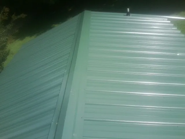New green metal panels meeting at the ridge of a roof — Flat Roof Repair work by our crew in East Pembroke