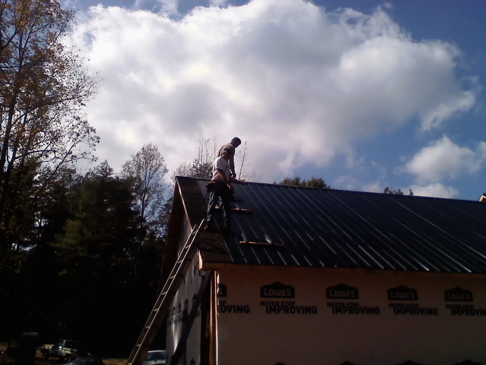 Roofer fastening dark metal panels high against a cloudy sky, from a Roof Inspection job in East Pembroke