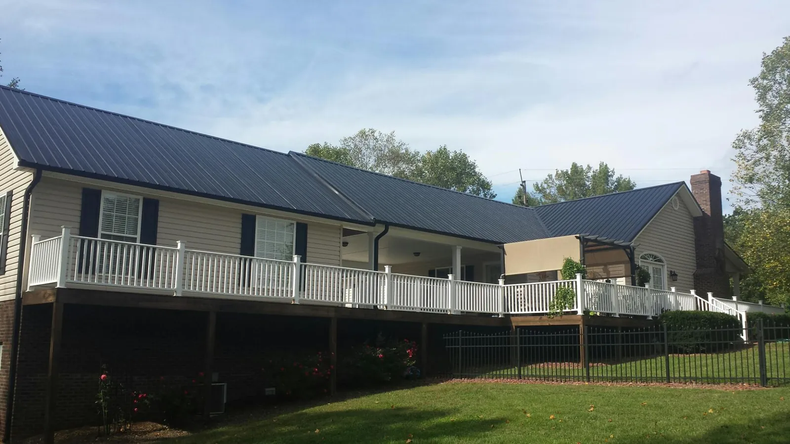 Black metal roof above a long white railed deck on a hillside home in East Pembroke
