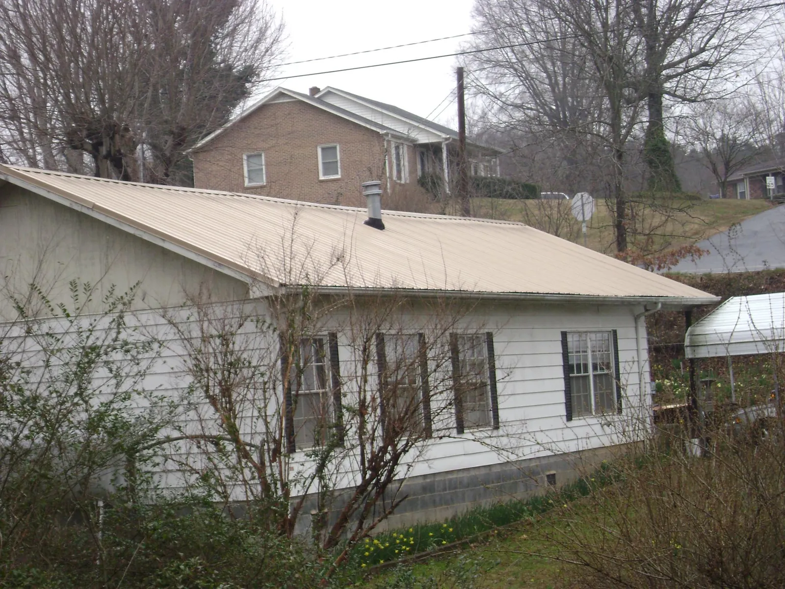 Tan metal roof on a white sided house set into a hillside — Commercial Roofing by Roofing Brothers in East Pembroke