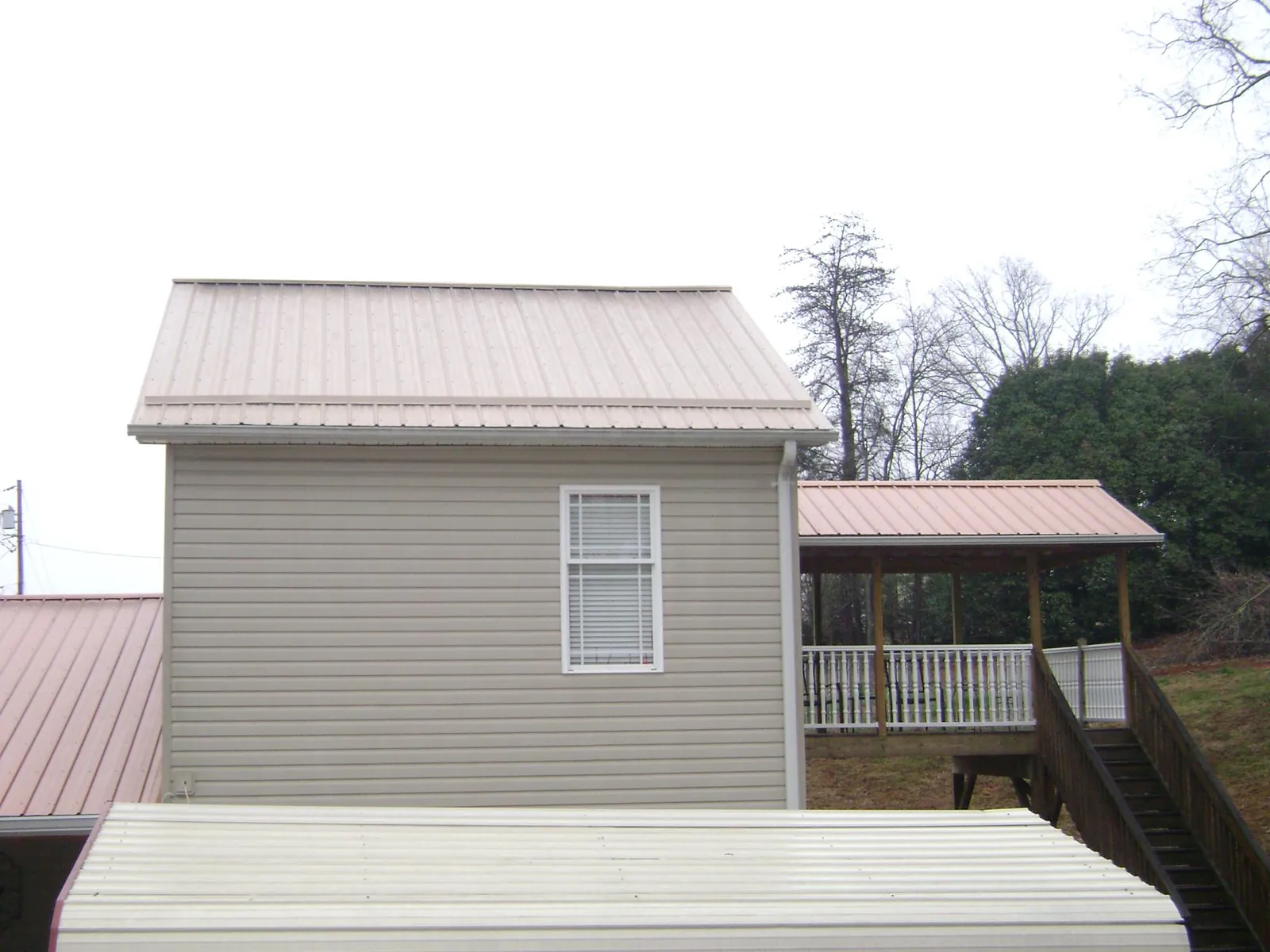 Tan metal roofs on a two story addition and attached porch, from a Roof Replacement job in East Pembroke